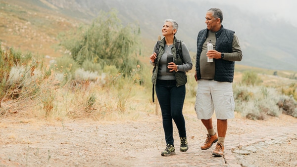 Happy, a man and woman walking in a natural landscape and drinking water. 