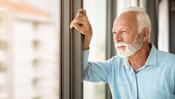 Serious senior man looking through window of his apartment.