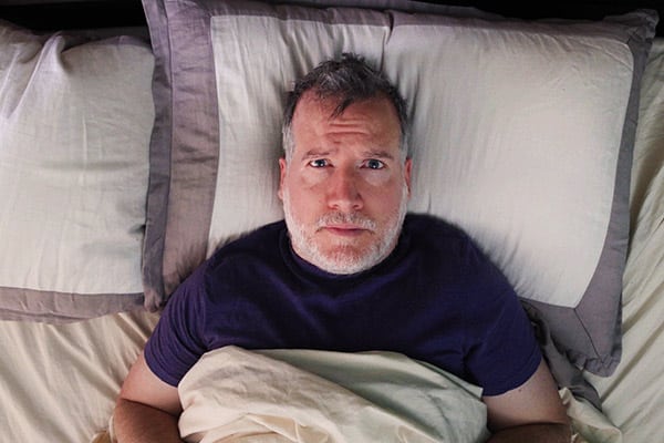 Mature man in bed struck with insomnia looking at camera with frustration