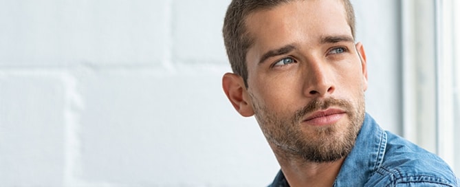 Thoughtful young man sitting near window and looking away.