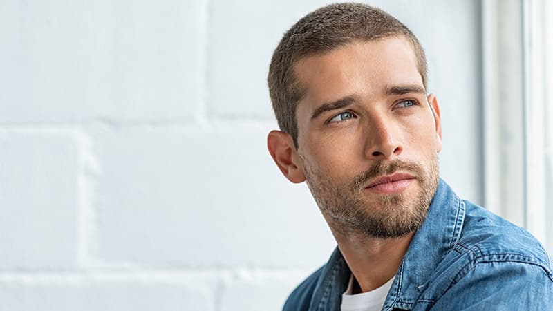 Thoughtful young man sitting near window and looking away.